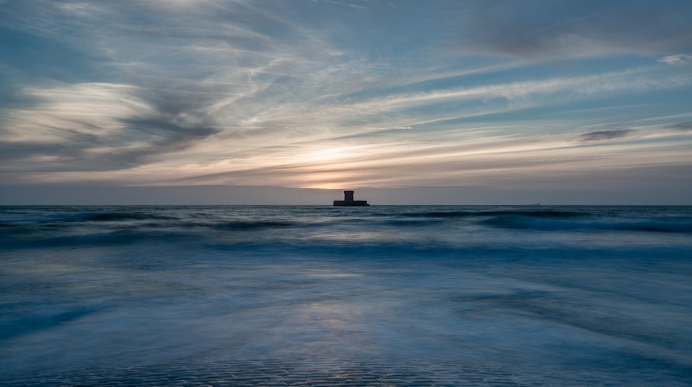 the sun is setting over the ocean with a lighthouse in the distance