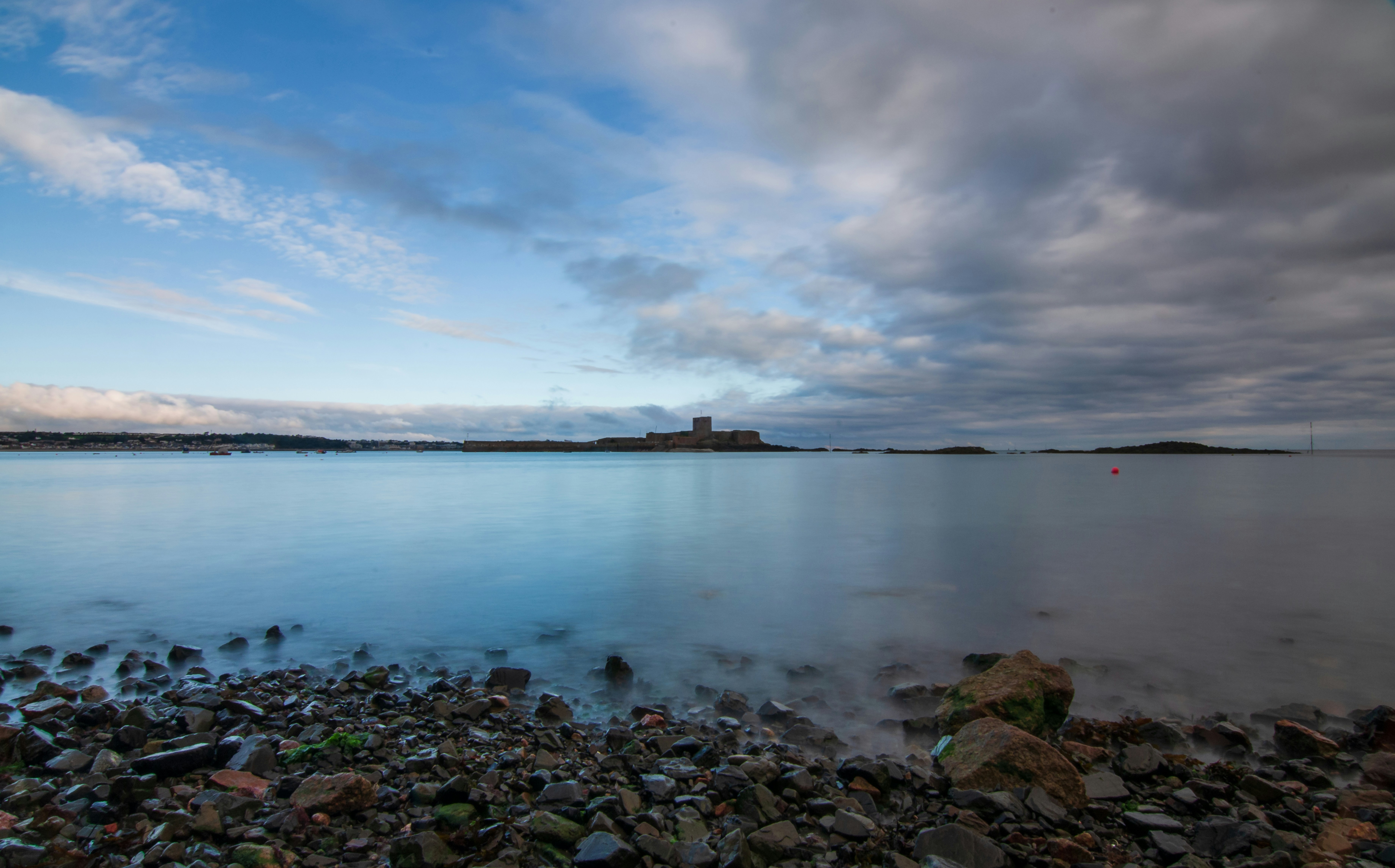 a large body of water surrounded by rocks, Long exposure of the seascape at St. Aubin