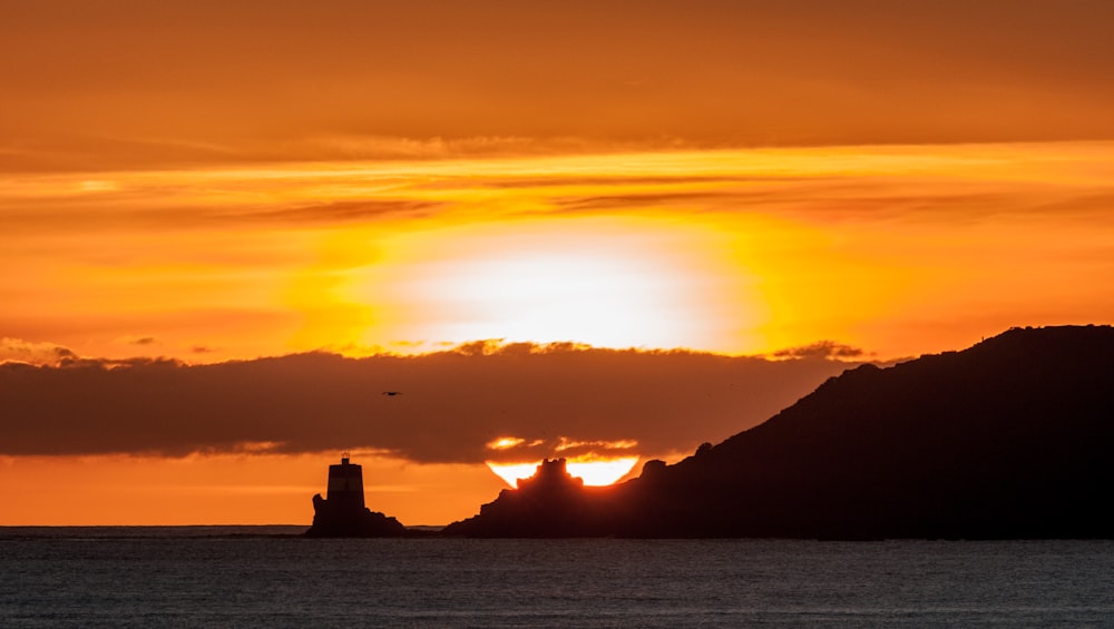 the sun is setting over the ocean with a lighthouse in the foreground