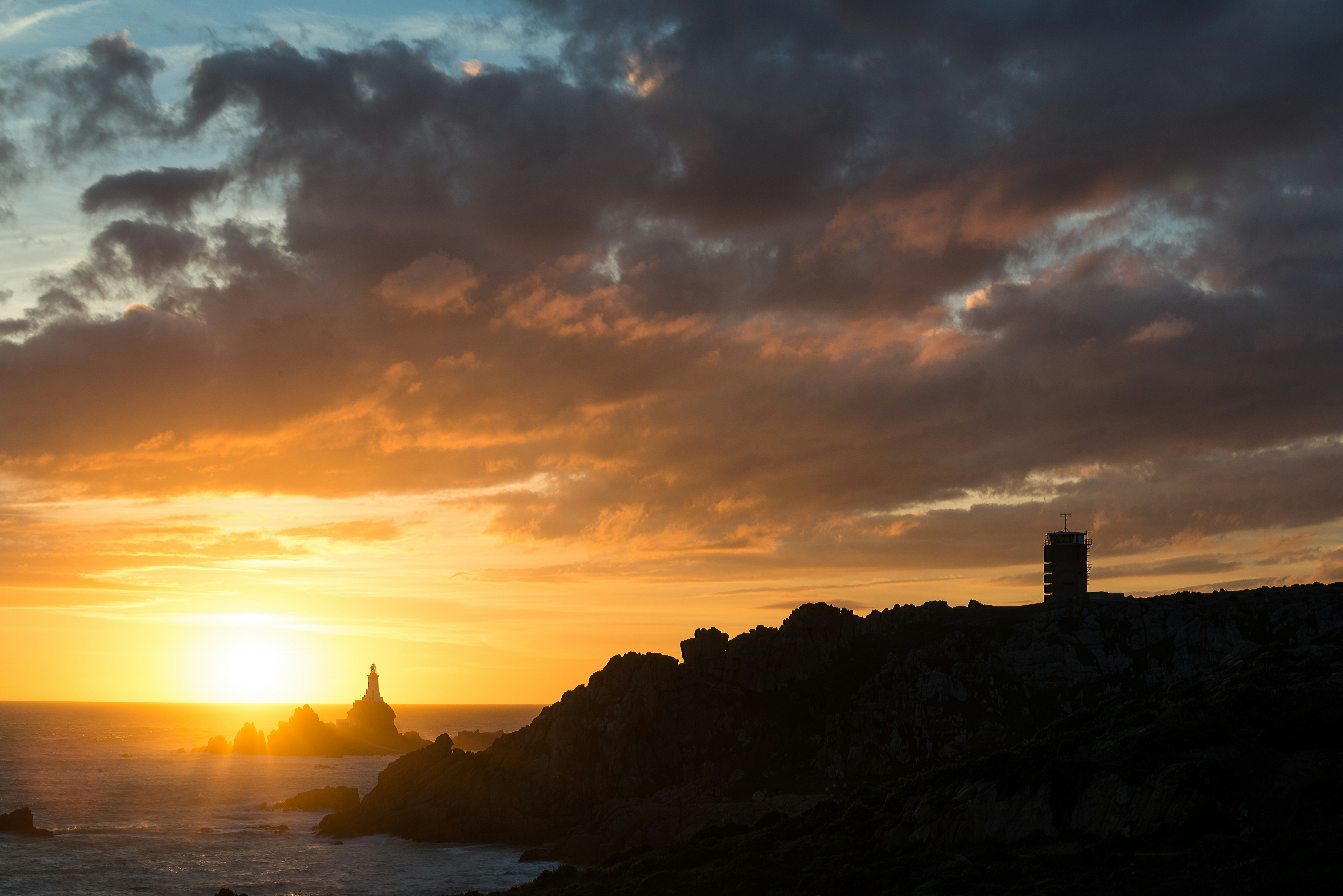 the sun is setting over the ocean with a lighthouse in the foreground