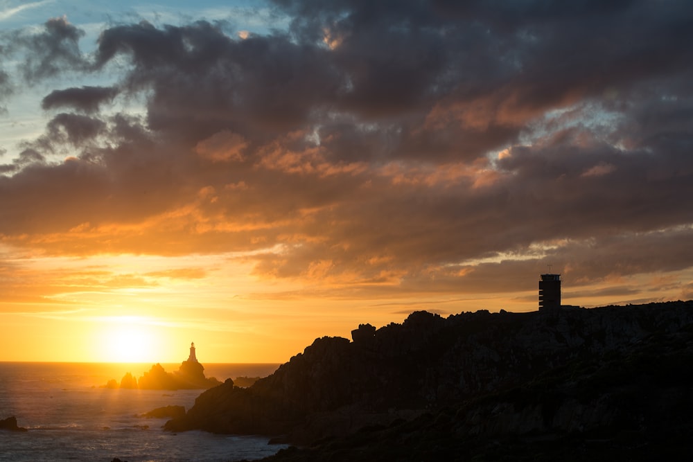 the sun is setting over the ocean with a lighthouse in the foreground