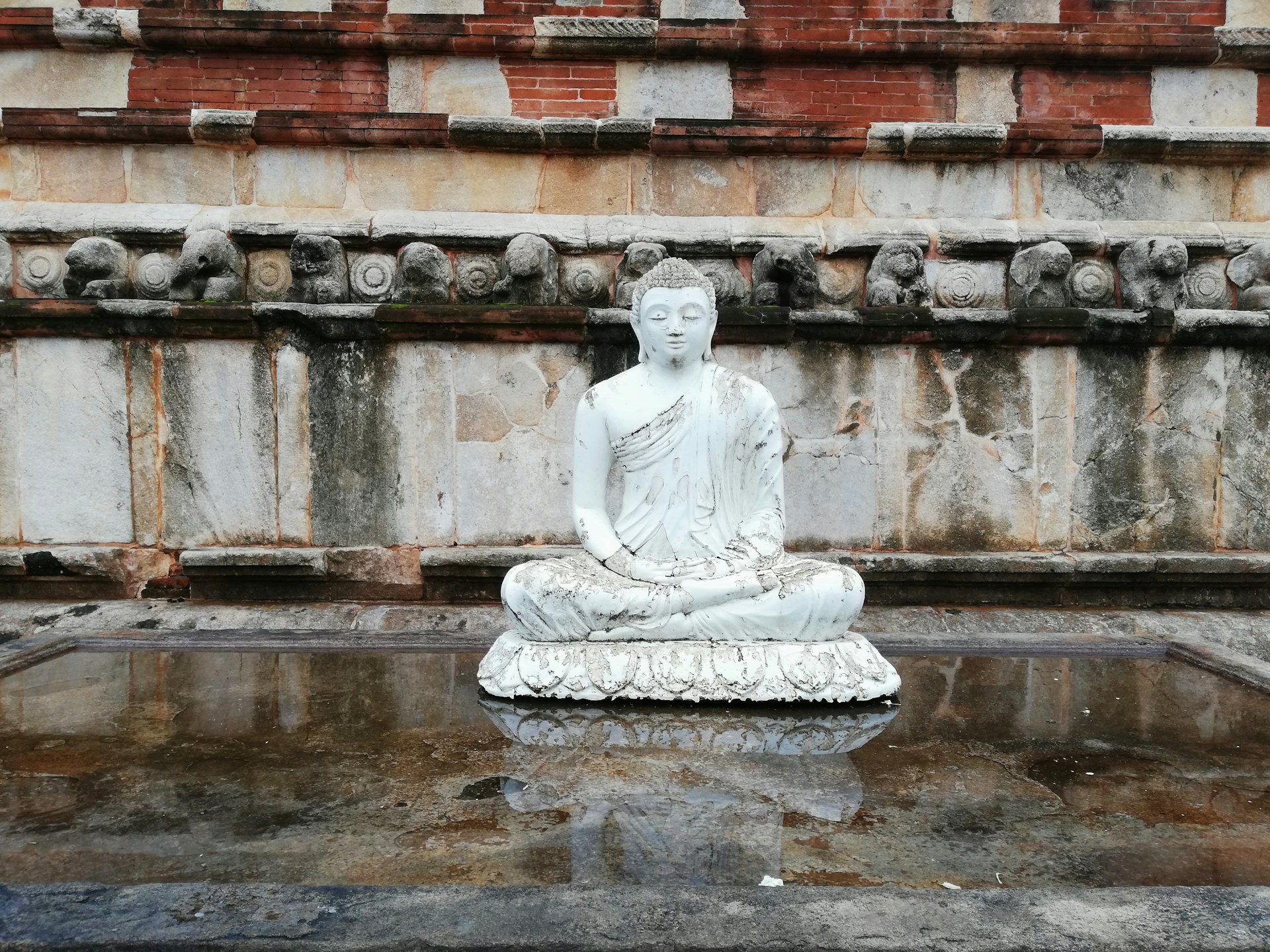 a white buddha statue sitting on top of a pool of water