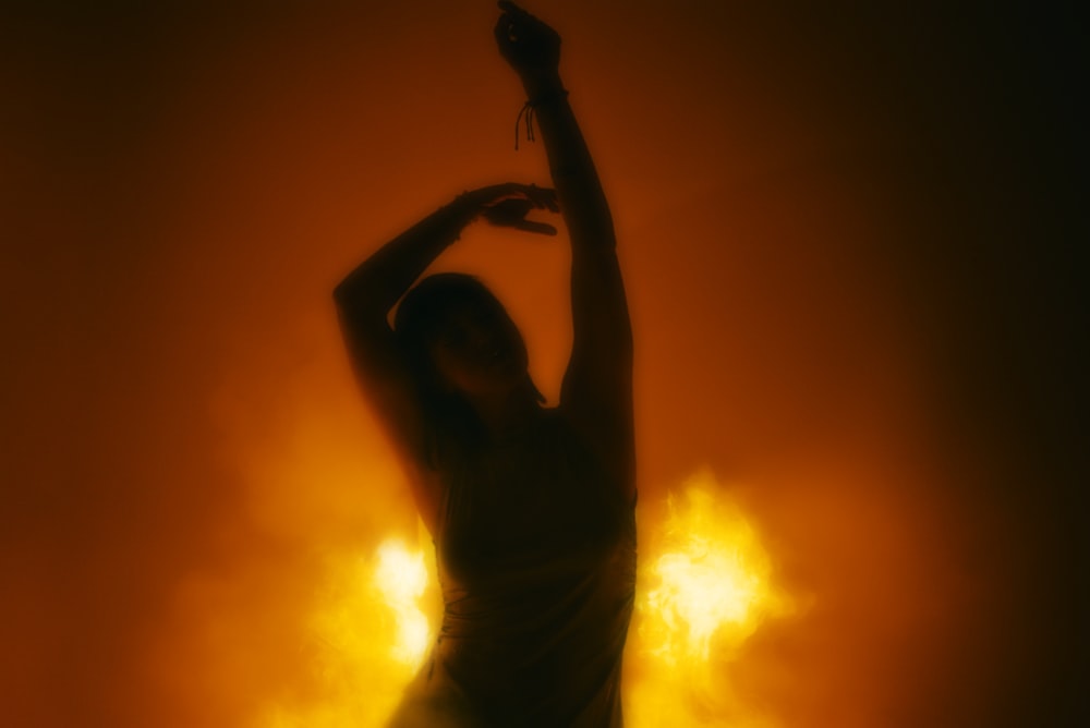 a woman is dancing in the dark with her arms in the air