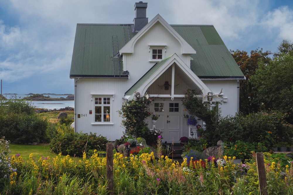 a white house with a green roof surrounded by flowers