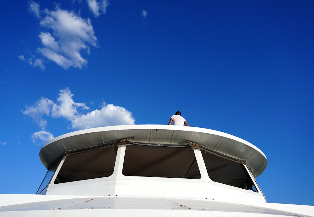 a man standing on top of a white boat under a blue sky
