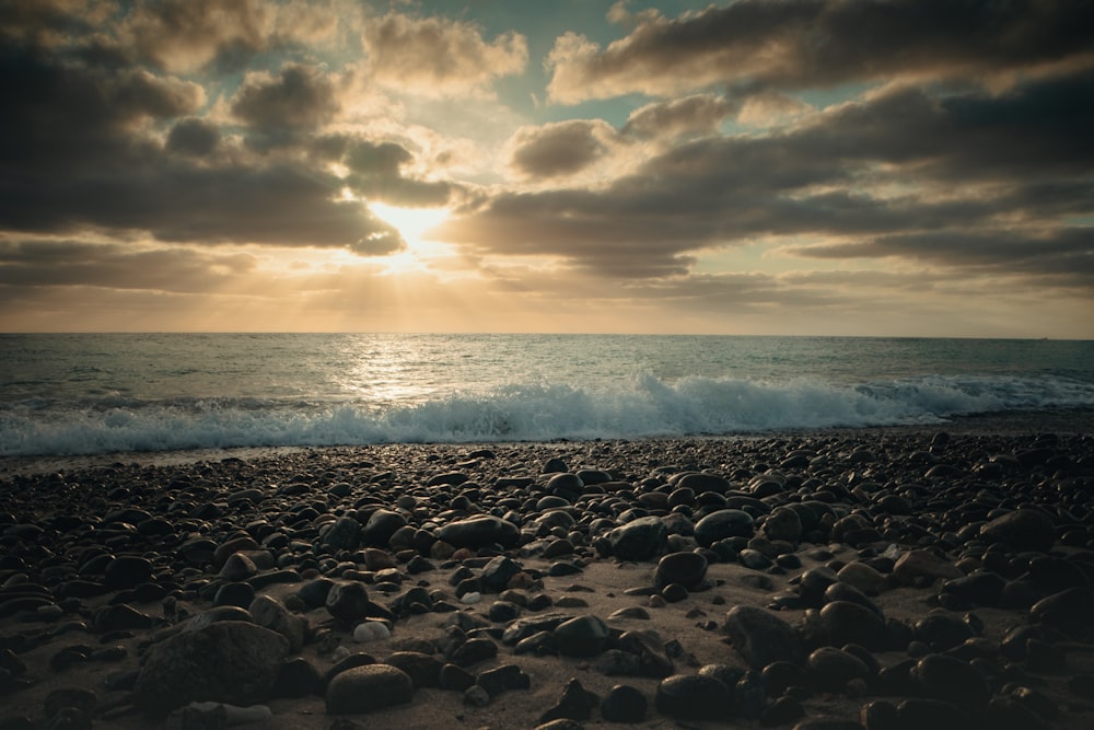 the sun is setting over the ocean on a rocky beach