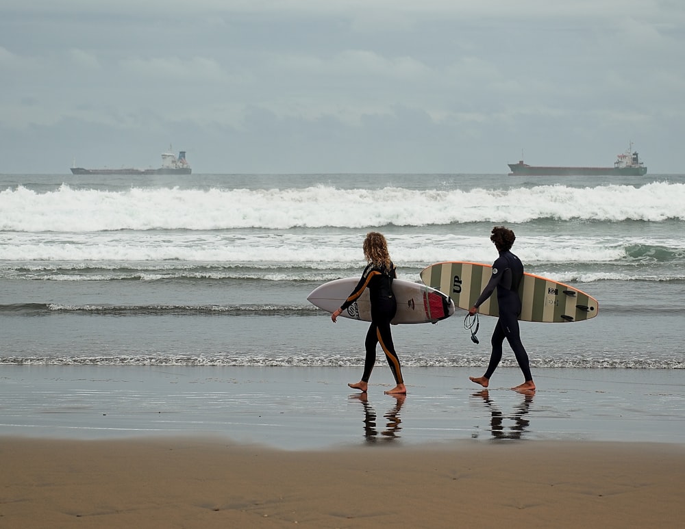 two people walking on the beach with surfboards