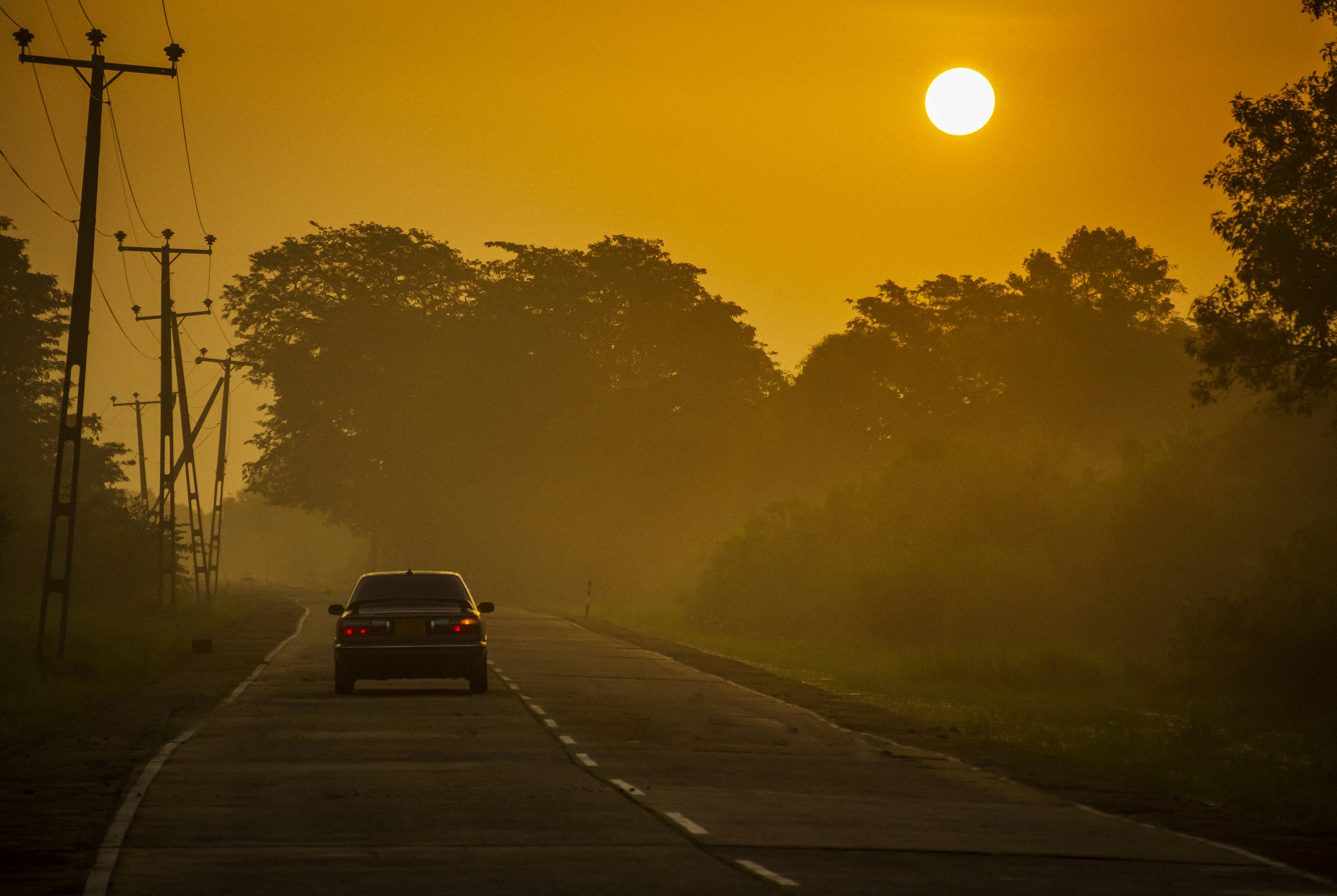 a car driving down a road with the sun in the background