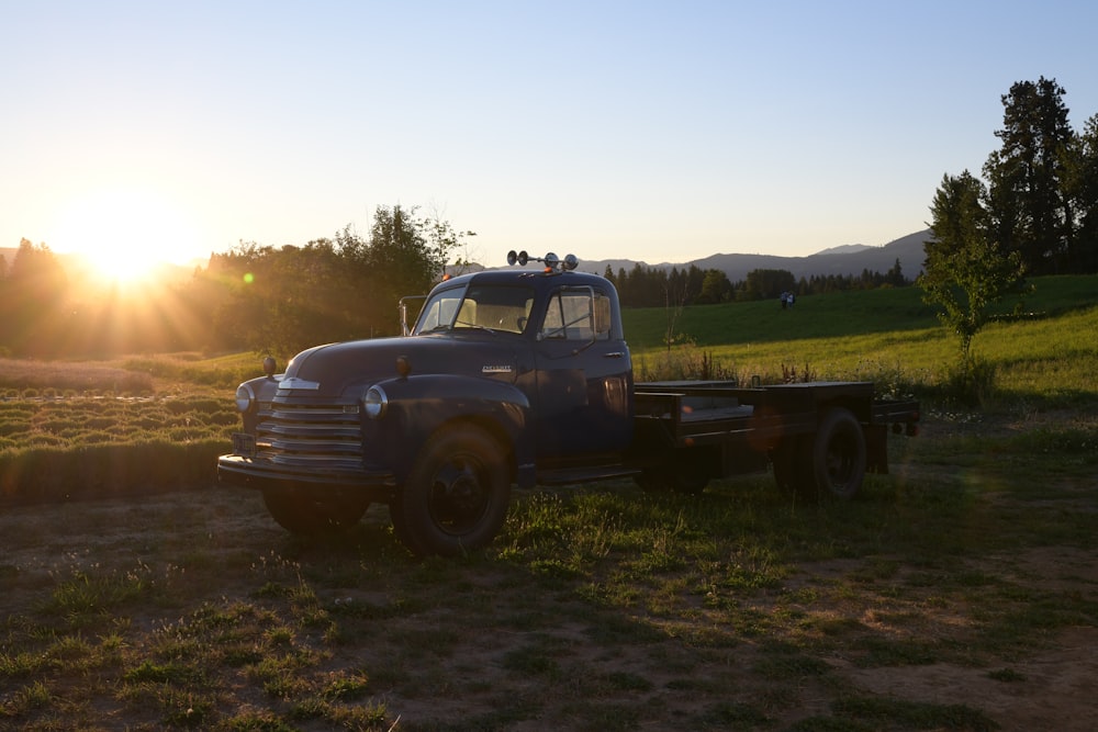 an old truck parked in a field at sunset
