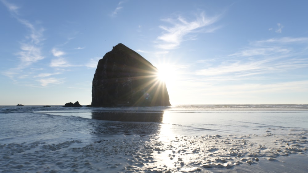 the sun shines brightly on a beach near a rock
