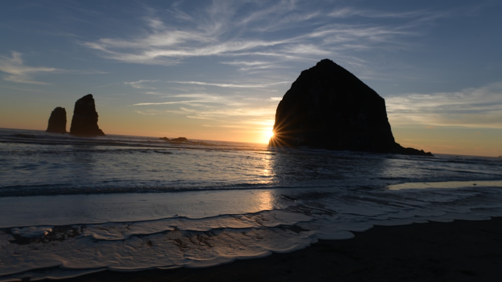 the sun is setting over the ocean with a rock formation in the distance