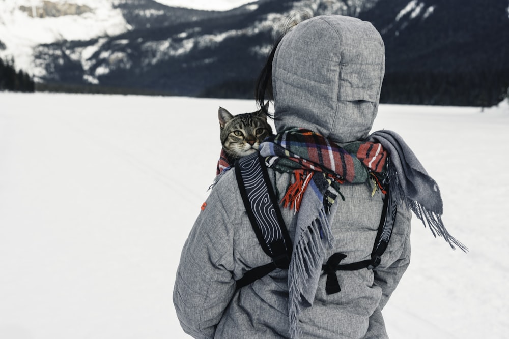 a person walking in the snow with a cat on their back