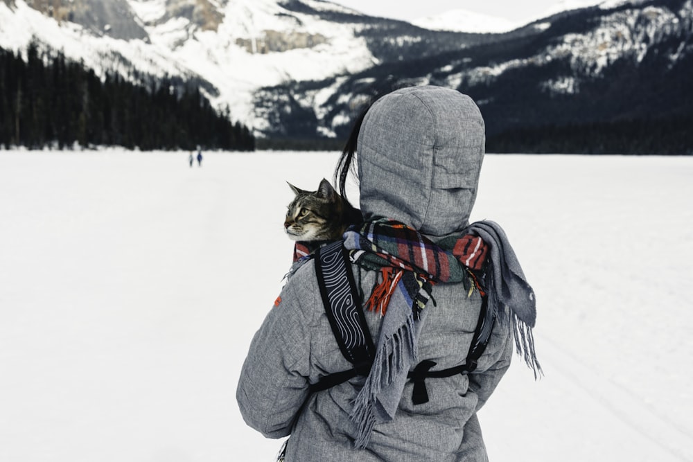 a person walking in the snow with a cat on their back