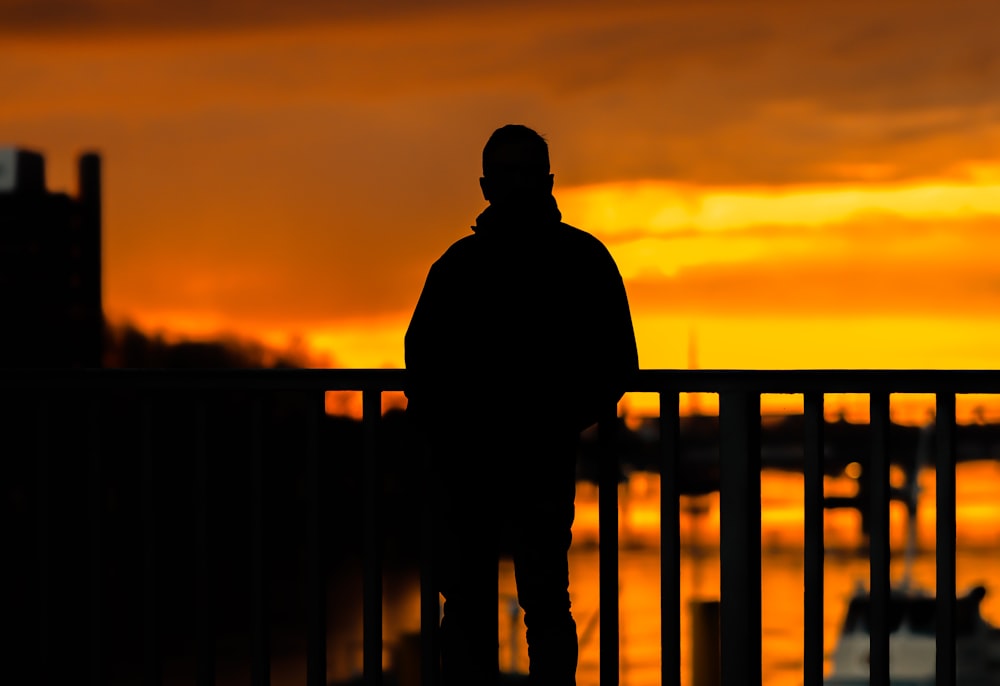a man standing on a bridge watching the sunset