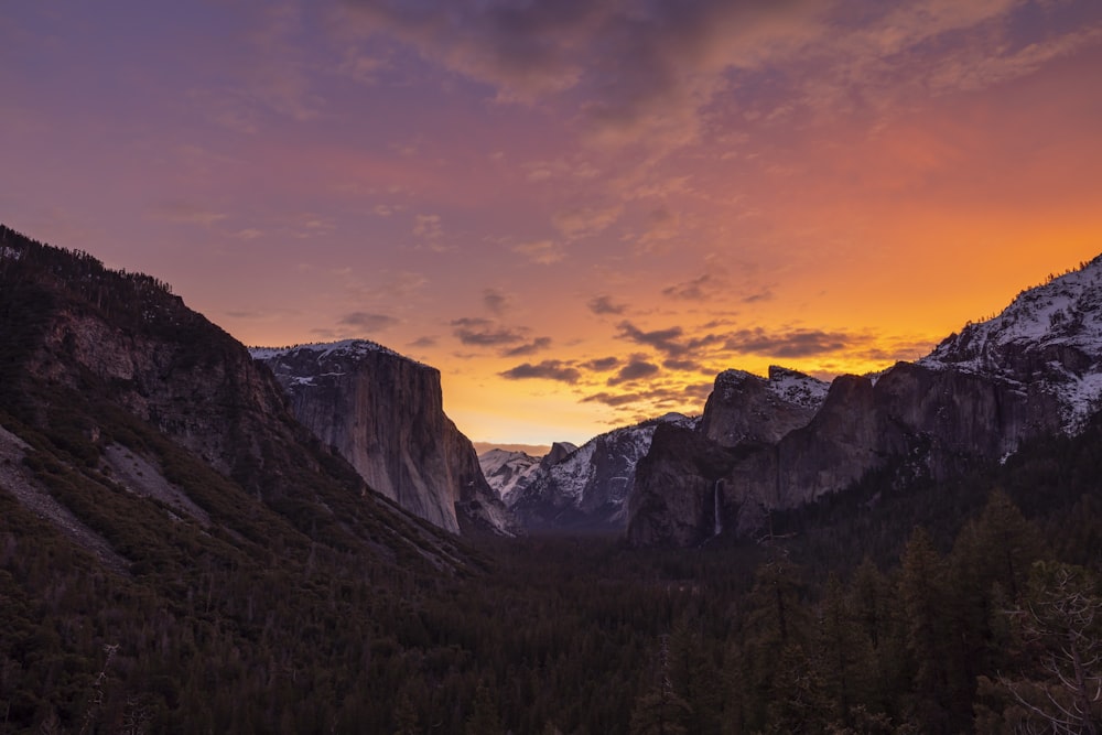 the sun is setting over the mountains and trees