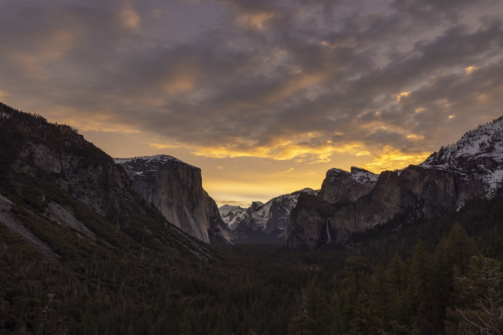 the sun is setting over the mountains and trees