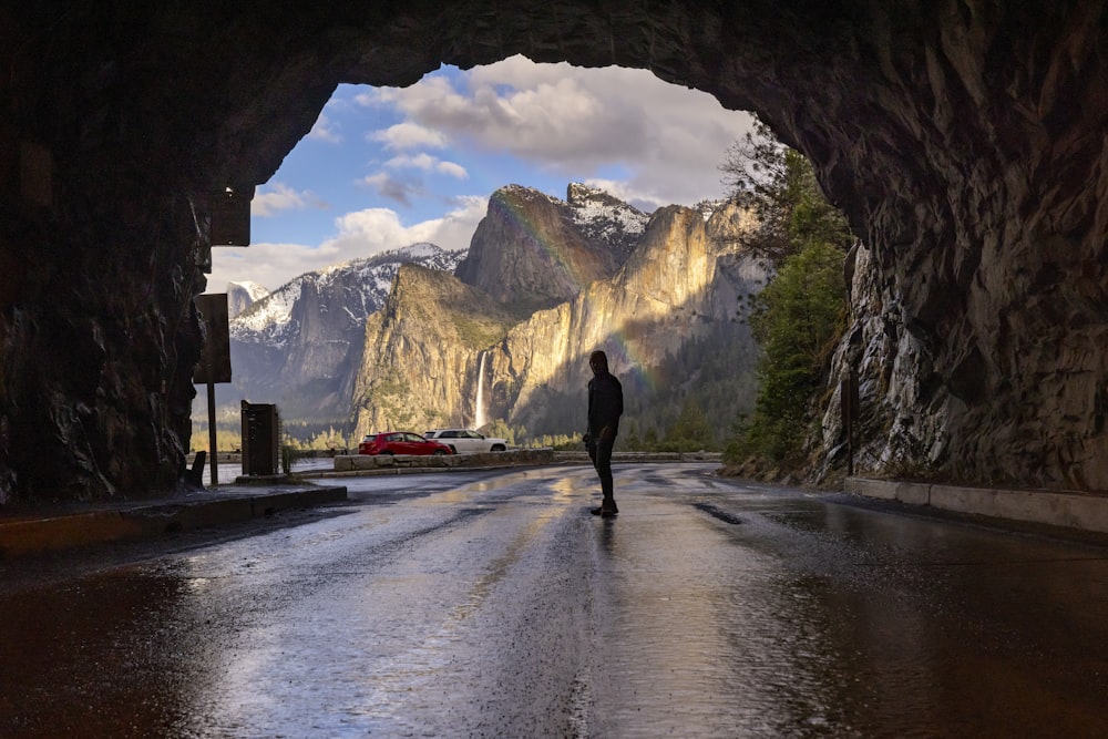 a person walking down a wet road under a tunnel