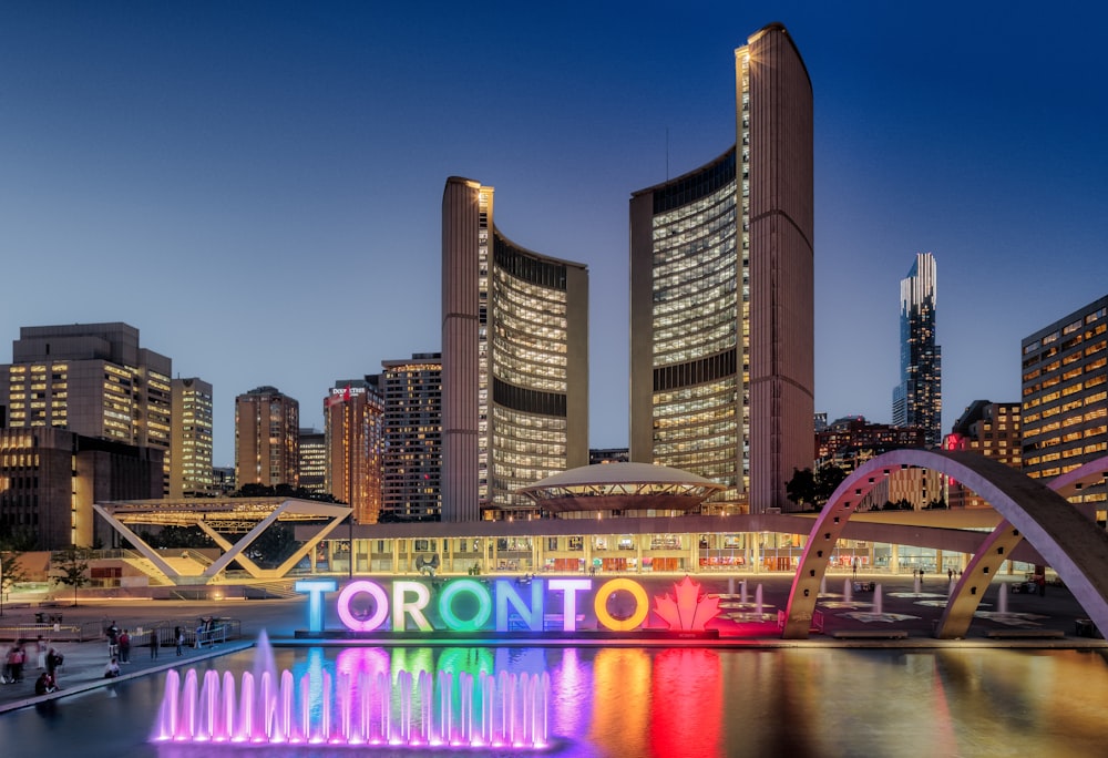 a city skyline with a rainbow fountain in the foreground