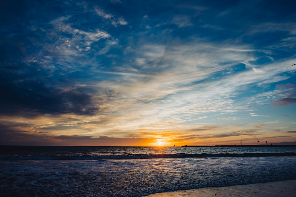 the sun is setting over the ocean on the beach