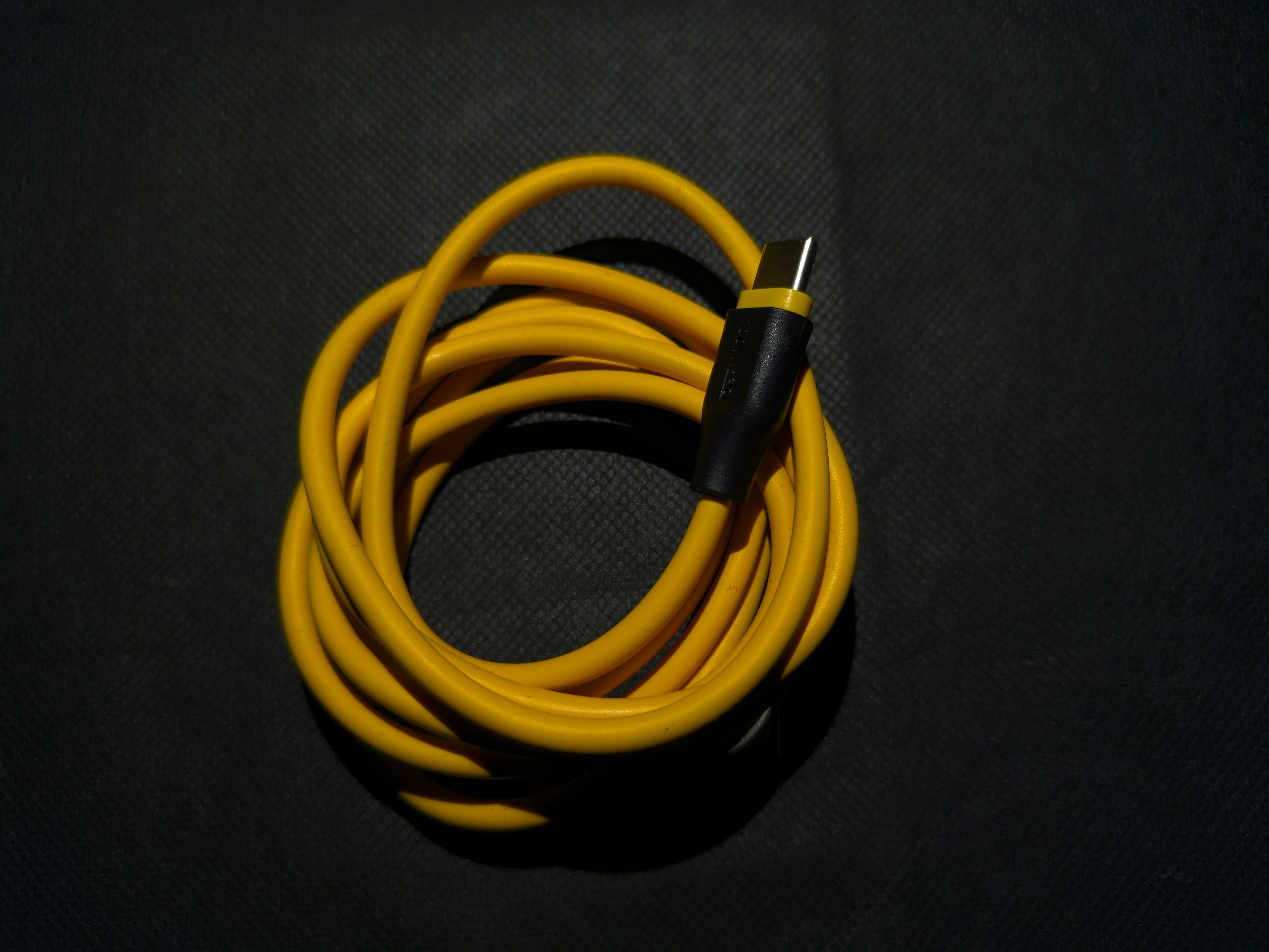 Modern USB-C charging cable coiled neatly on dark surface, electric blue glow, premium tech product