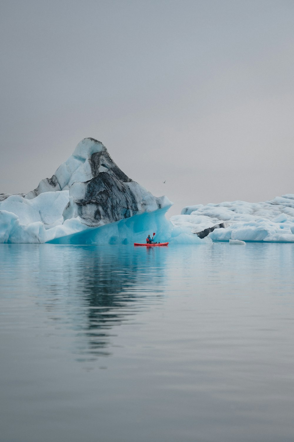 uma pessoa em um caiaque em frente a um iceberg