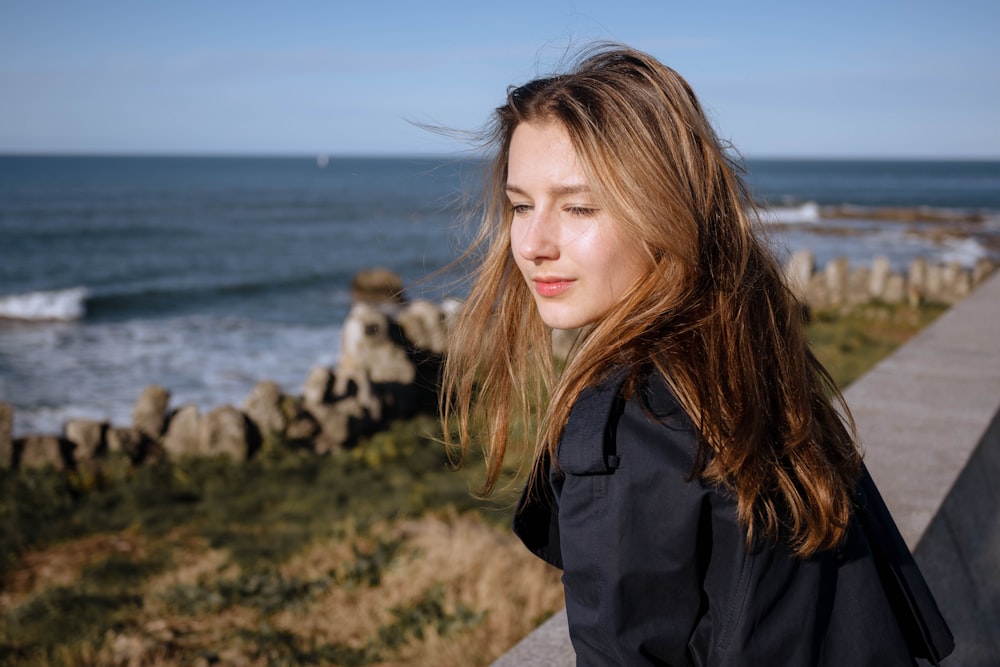 a woman with long hair standing next to the ocean