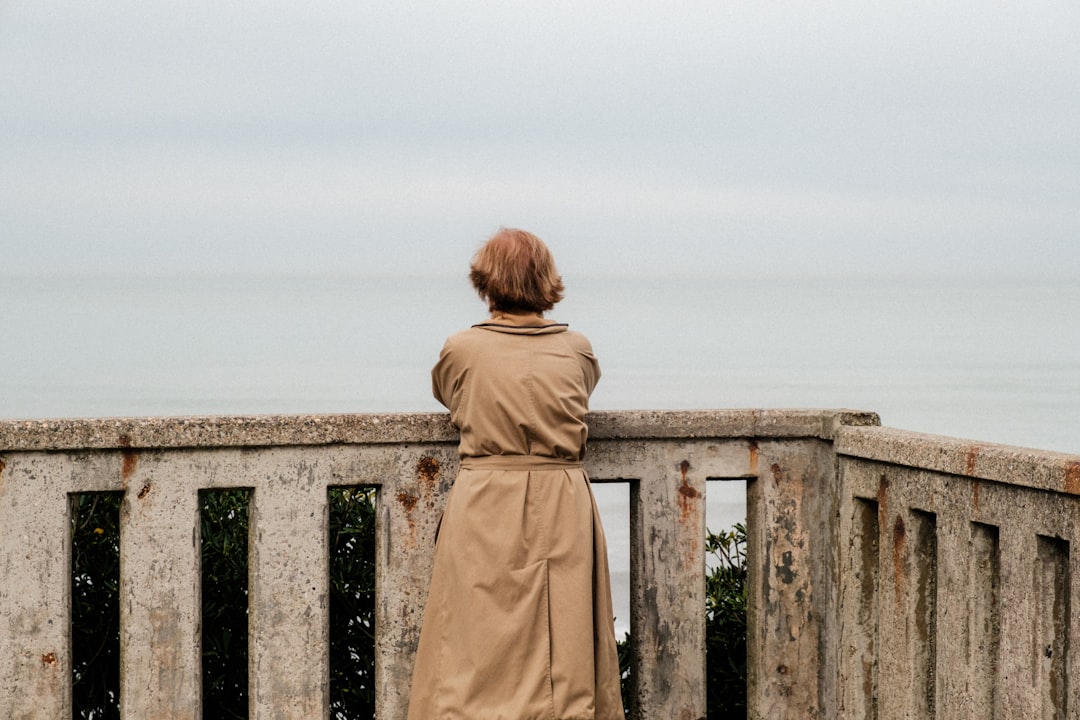a woman in a trench coat looking out over the ocean