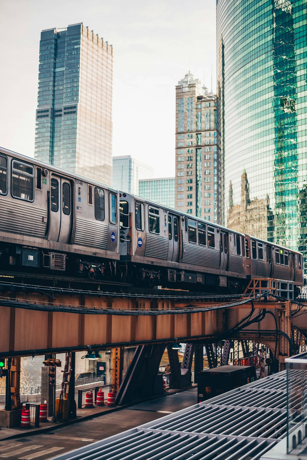 a silver train traveling over a bridge next to tall buildings