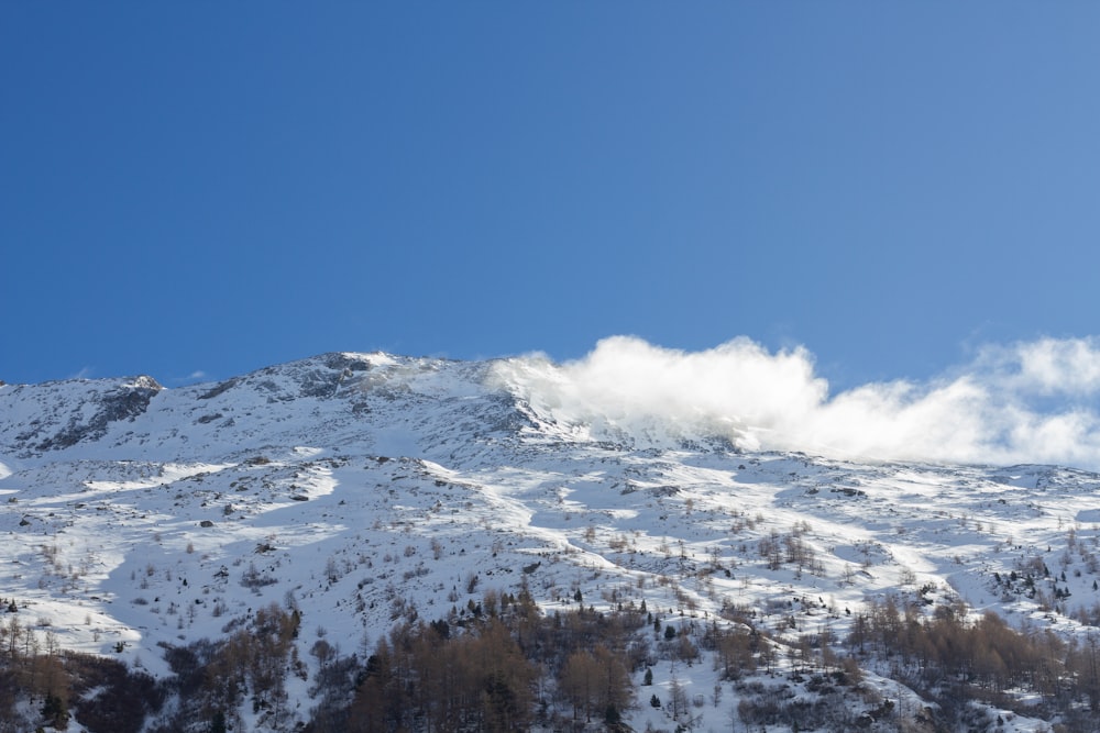 a mountain covered in snow and clouds under a blue sky