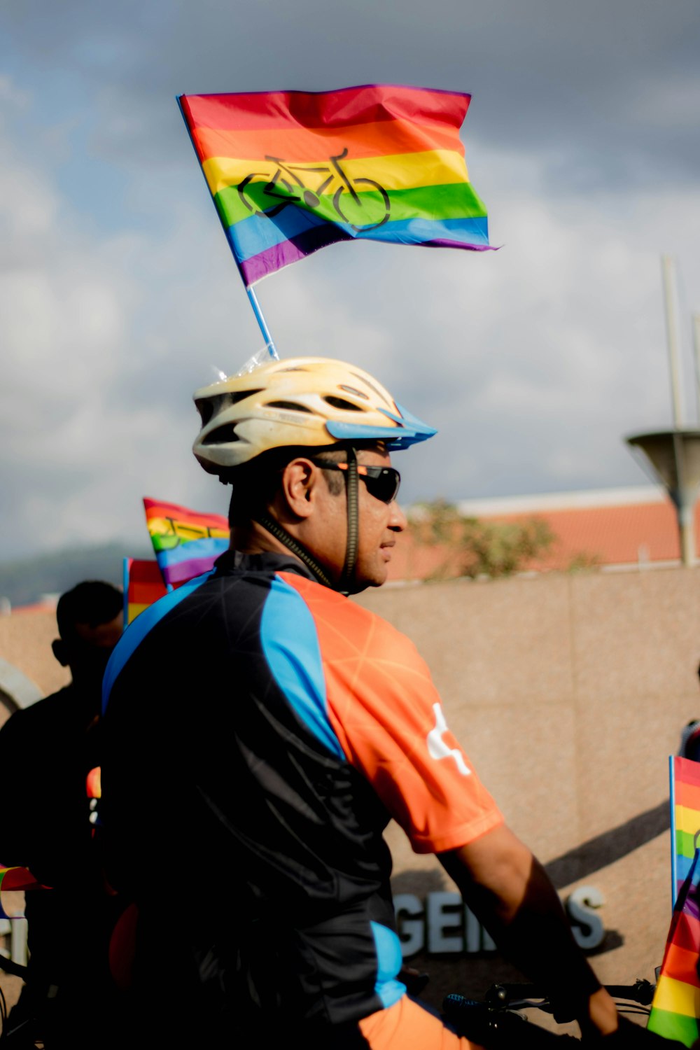 un uomo in sella a una bicicletta con in mano una bandiera arcobaleno