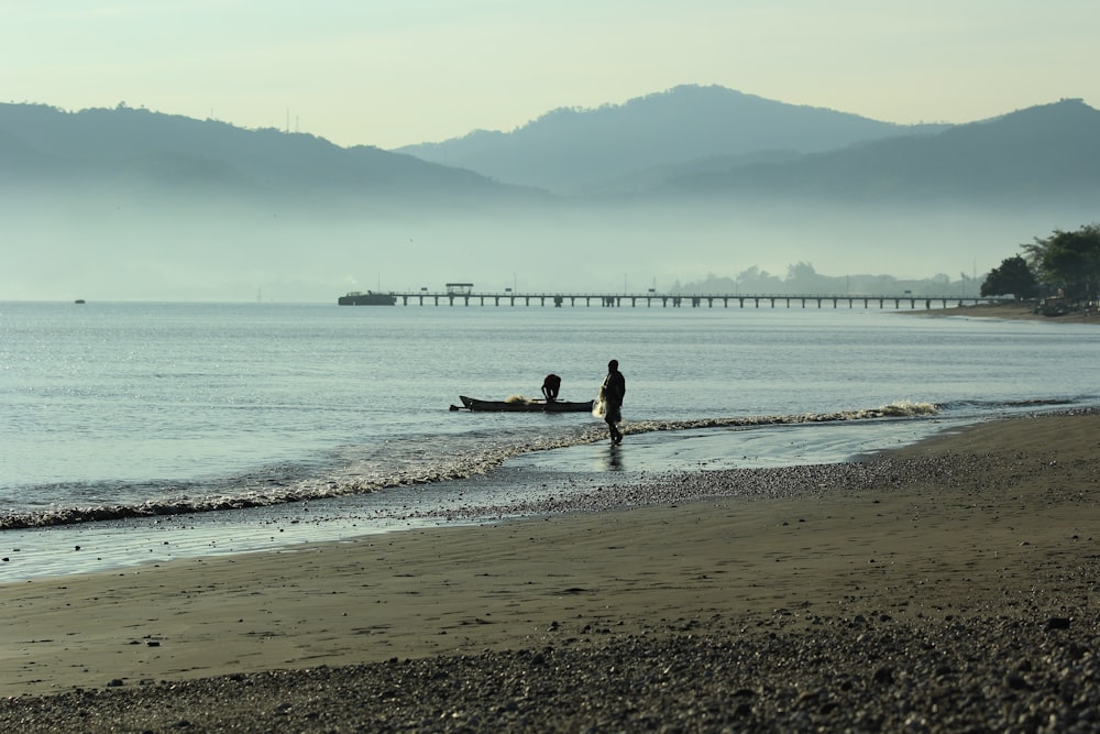 Un par de personas de pie en una playa junto a un barco