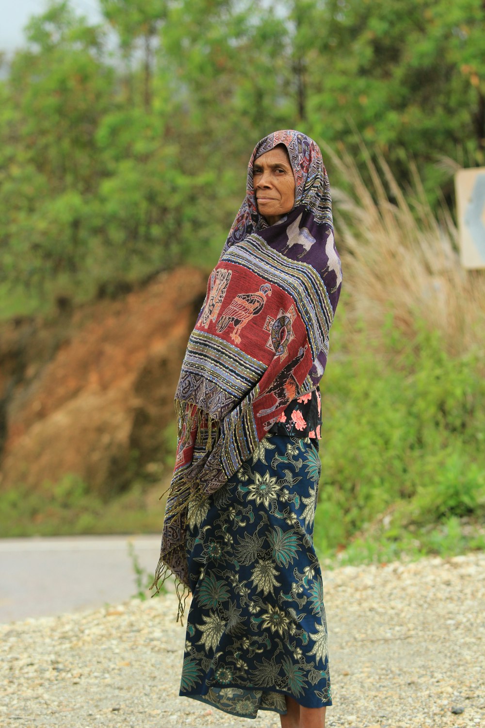 a woman in a colorful shawl standing on a gravel road