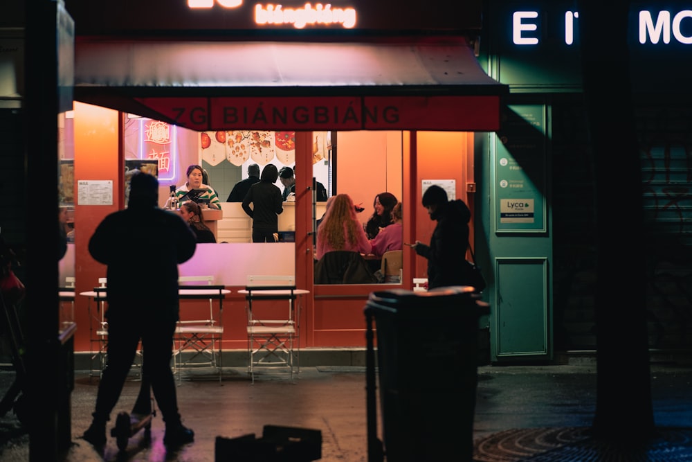 a group of people standing outside of a restaurant at night