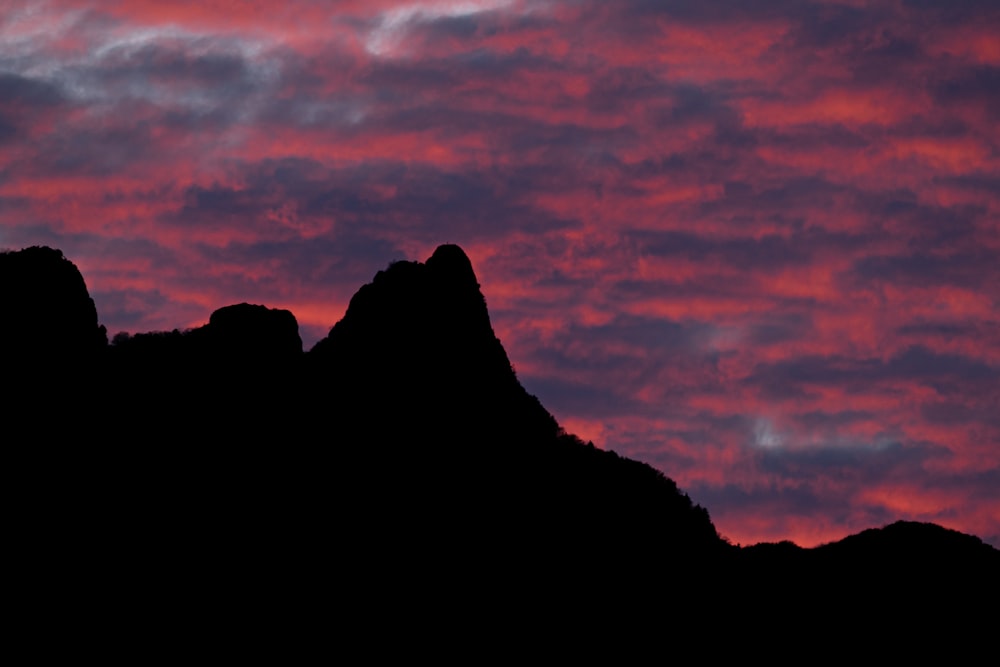 the silhouette of a mountain against a pink sky