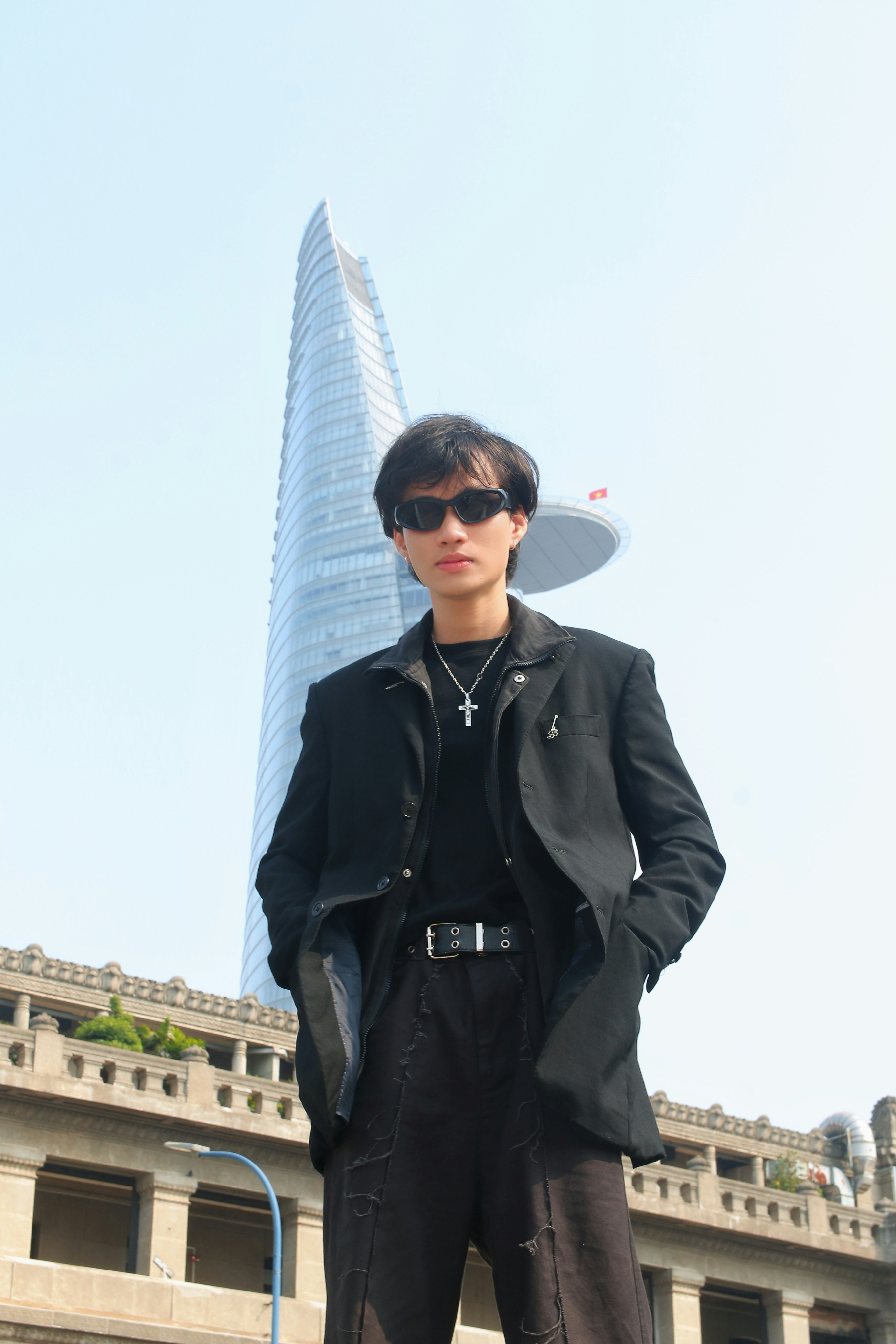 Stylish man in dark urban outfit, city background, confident pose, moody atmospheric lighting
