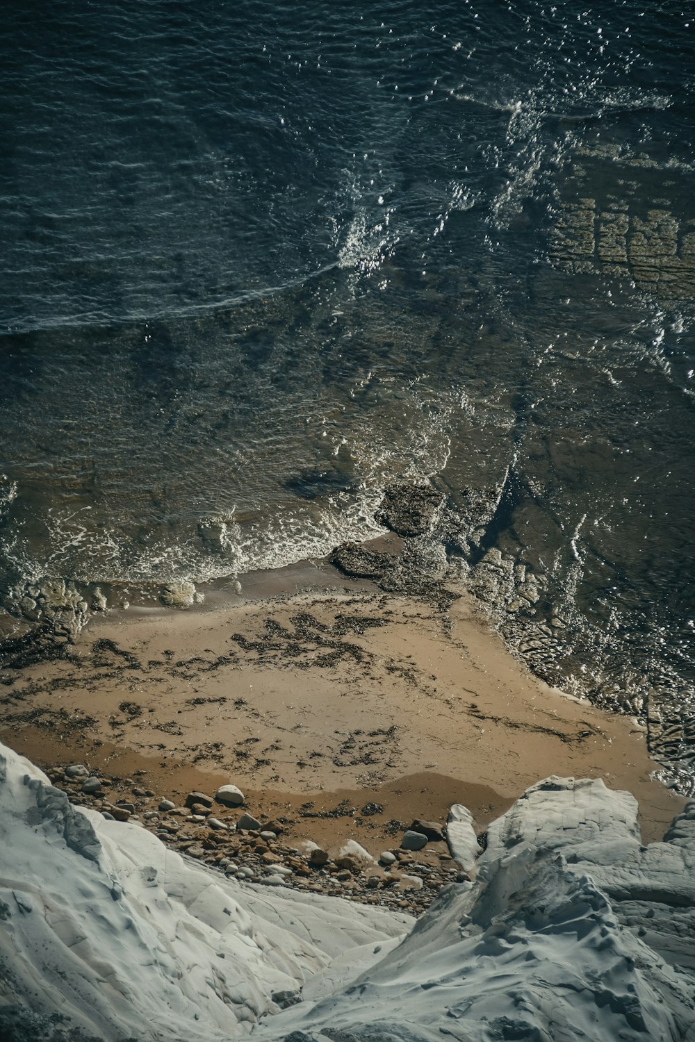 a sandy beach covered in snow next to the ocean