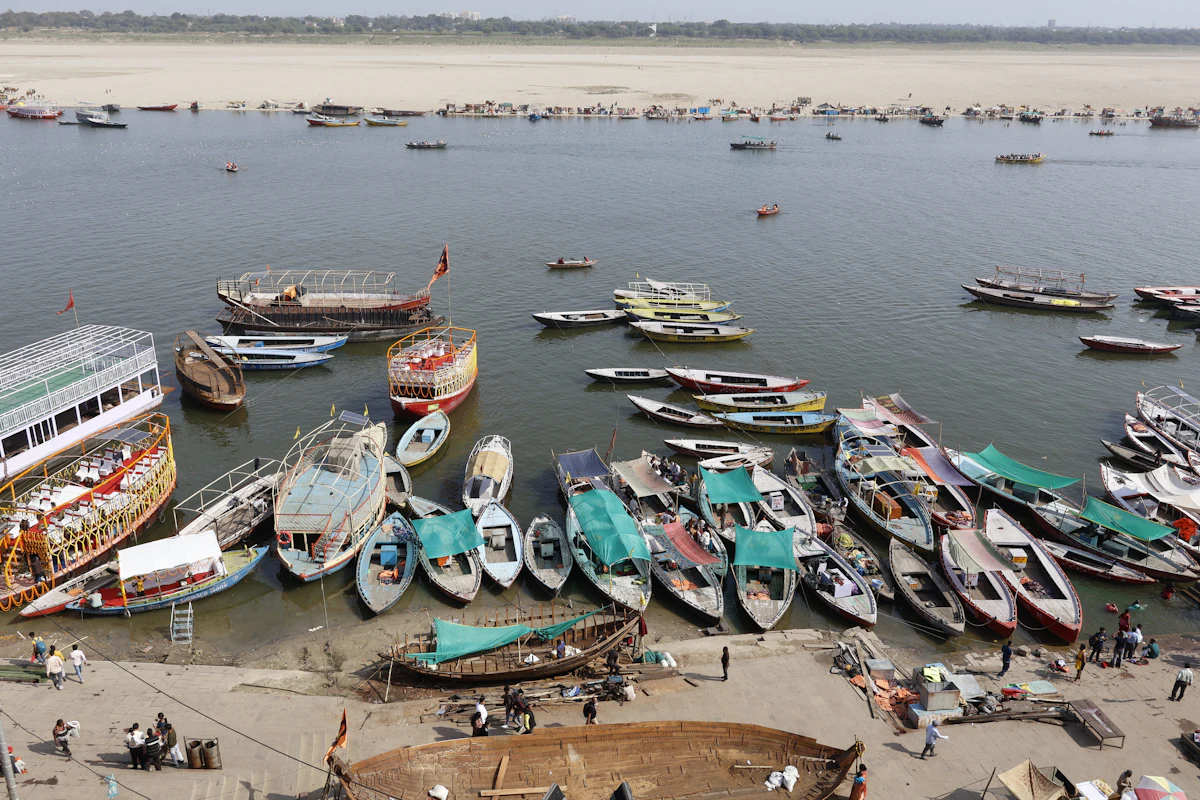 Rows of wooden rowing boats and larger motorboats moored on the Ganga below Dashashwamedh Ghat in Varanasi, with the sandy far bank beyond