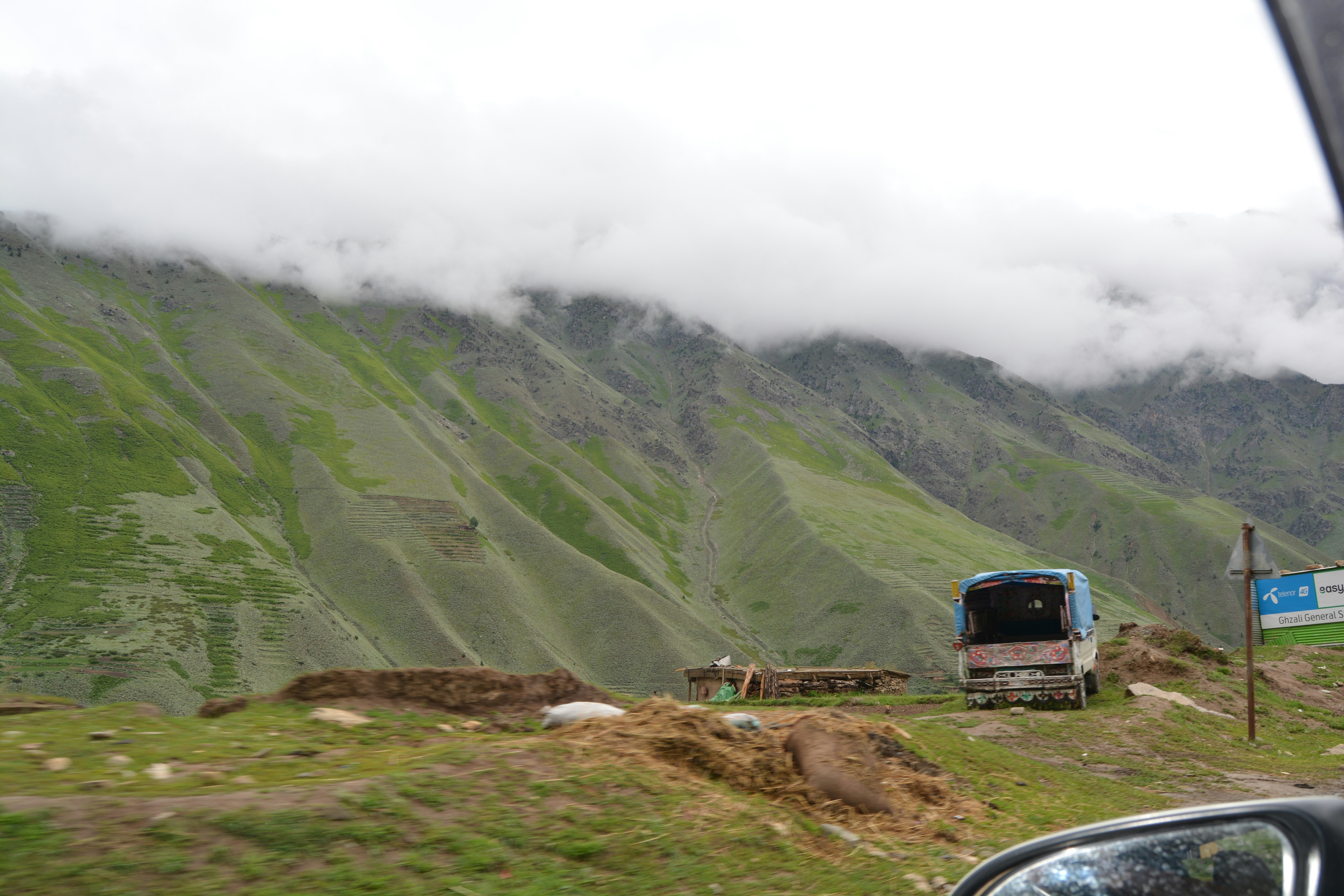 a truck driving down a road next to a lush green mountain