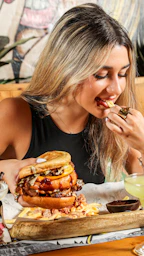 a woman sitting at a table eating a large sandwich