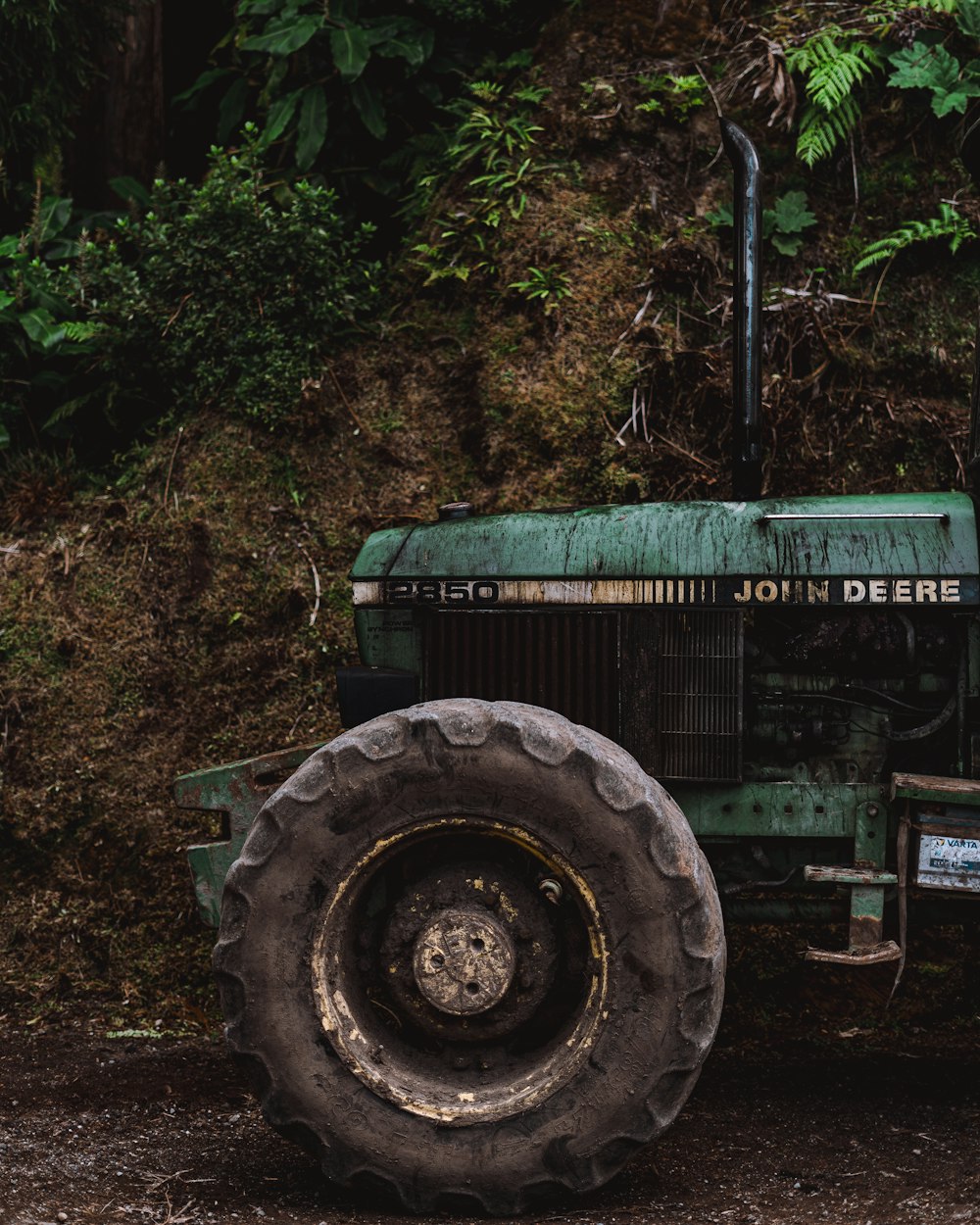 an old green tractor parked in front of a lush green hillside