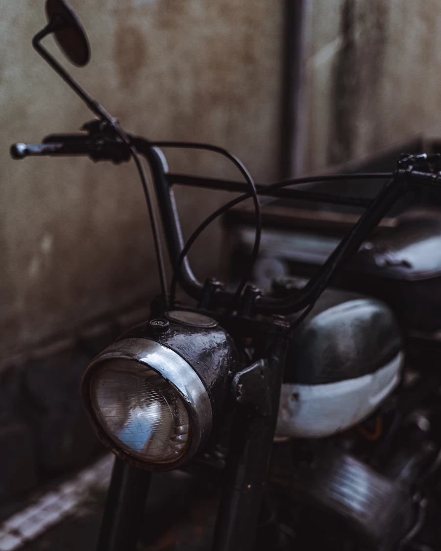 A vintage motorcycle headlight and handlebars in low light against a rusted wall