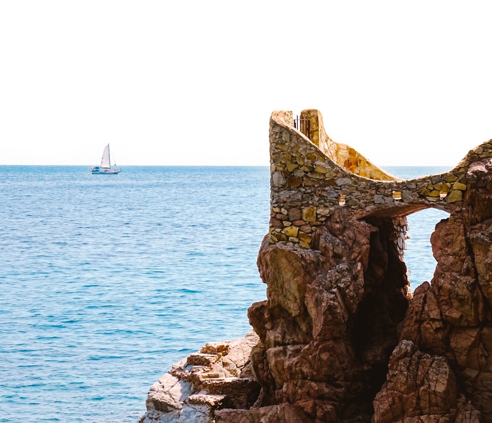 a rock formation with a sailboat in the distance