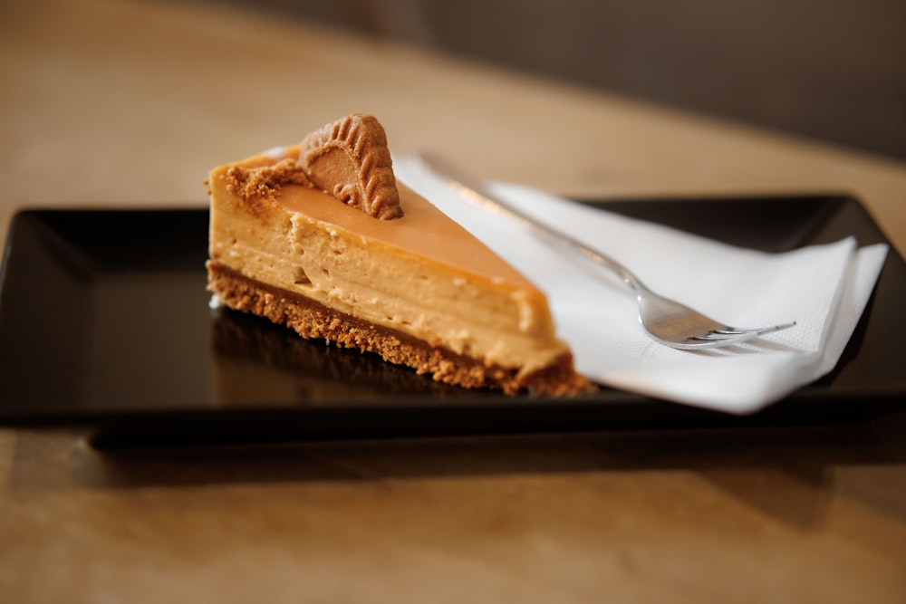 a piece of cheesecake on a black plate with a fork