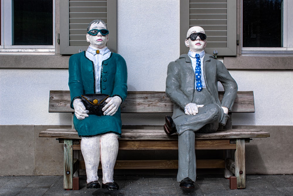 a couple of statues sitting on top of a wooden bench