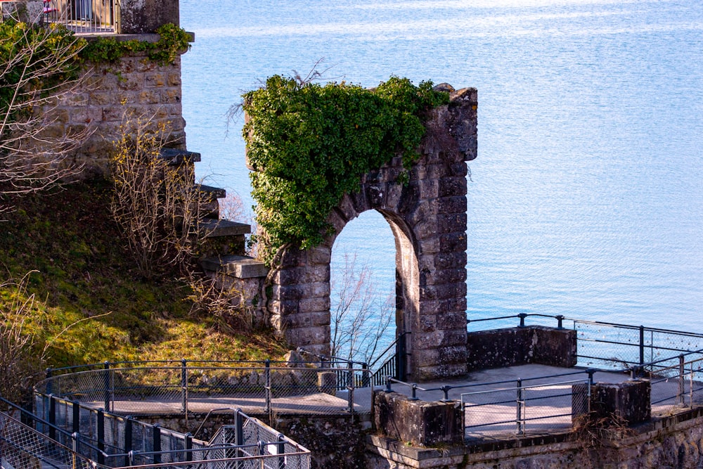 a stone structure with vines growing on it next to a body of water