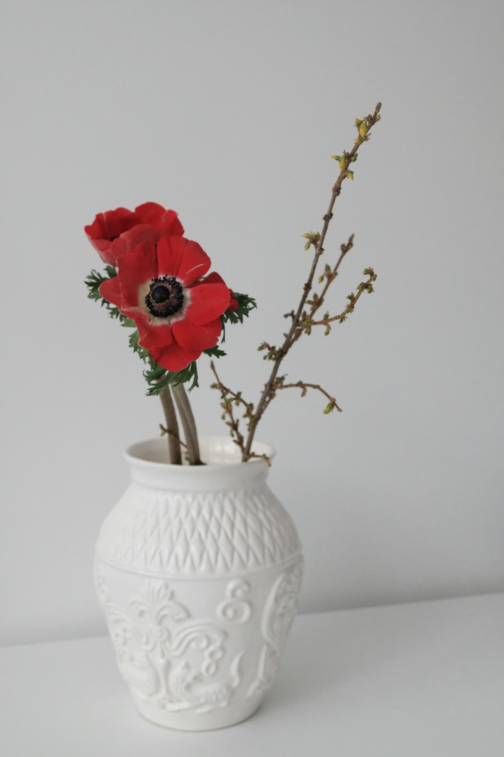 a white vase with some red flowers in it