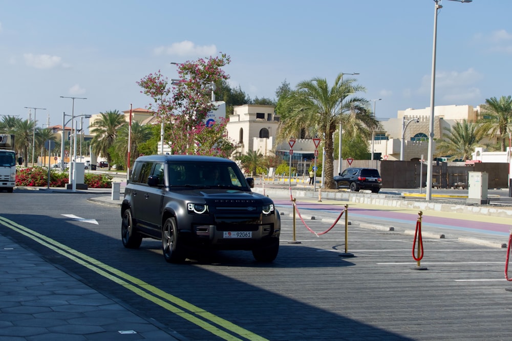 a black suv driving down a street next to palm trees