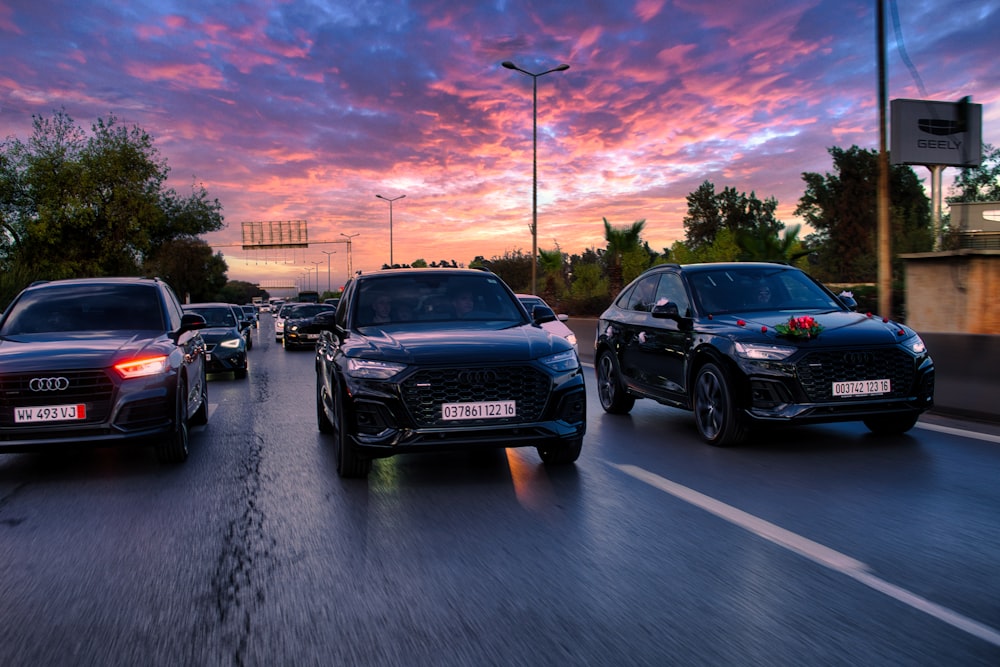 um grupo de carros dirigindo por uma rua ao pôr do sol