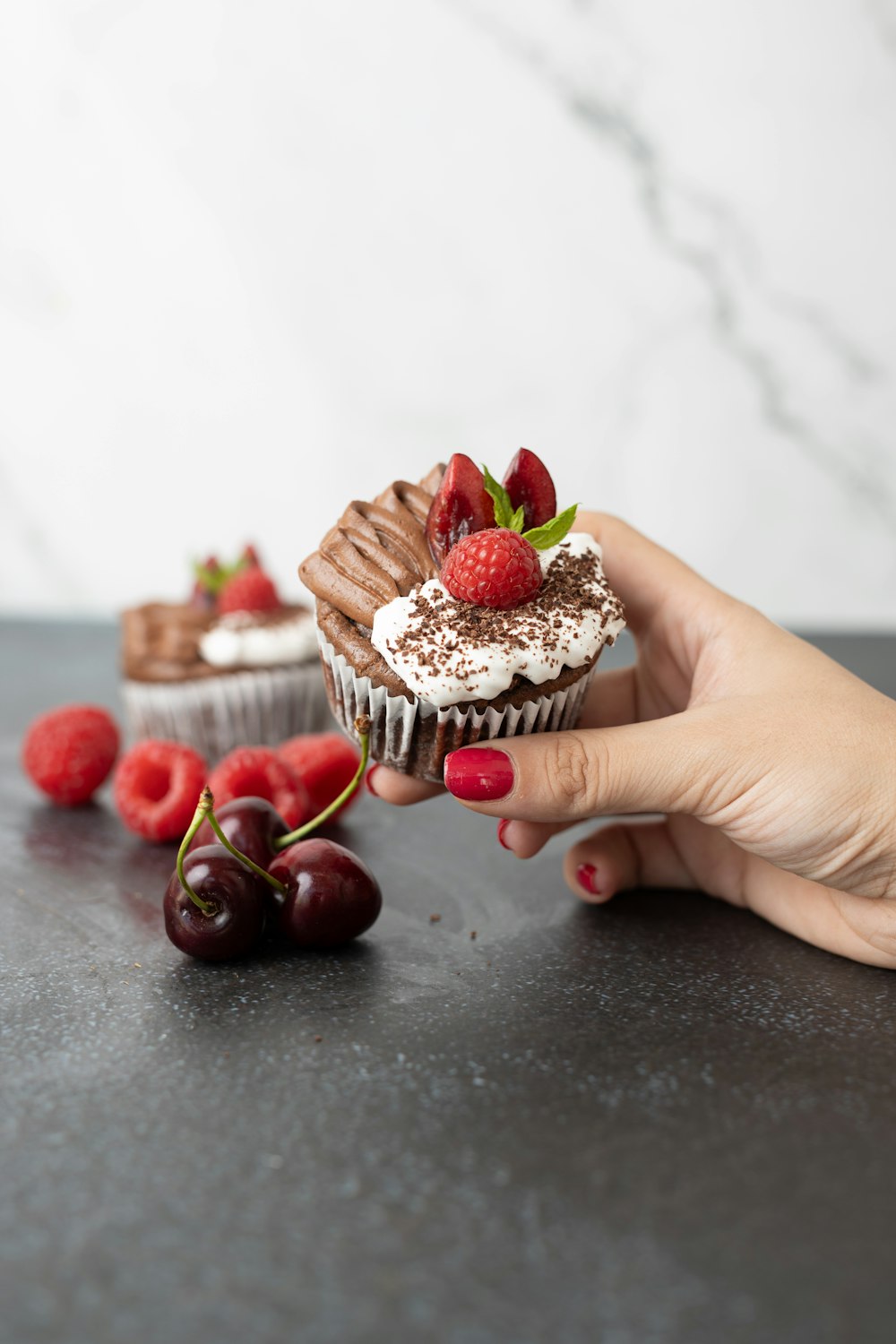 a hand holding a cupcake with chocolate frosting and strawberries