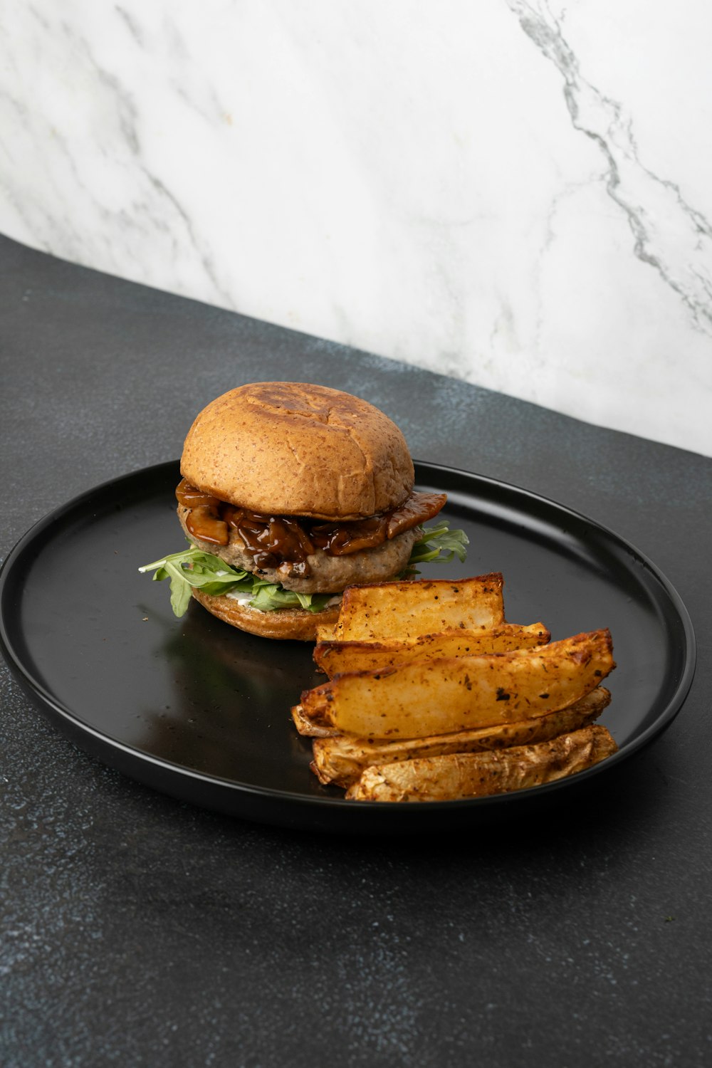 a black plate with a sandwich and some potato wedges